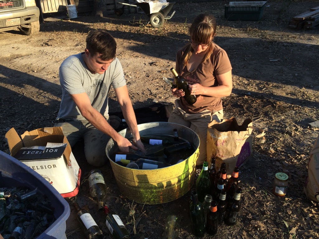 bottles must first have their labels removed, before being cut in half, taped to a matching size bottom, and mortared into the walls - here Seth & Kristin work the de-labelling step